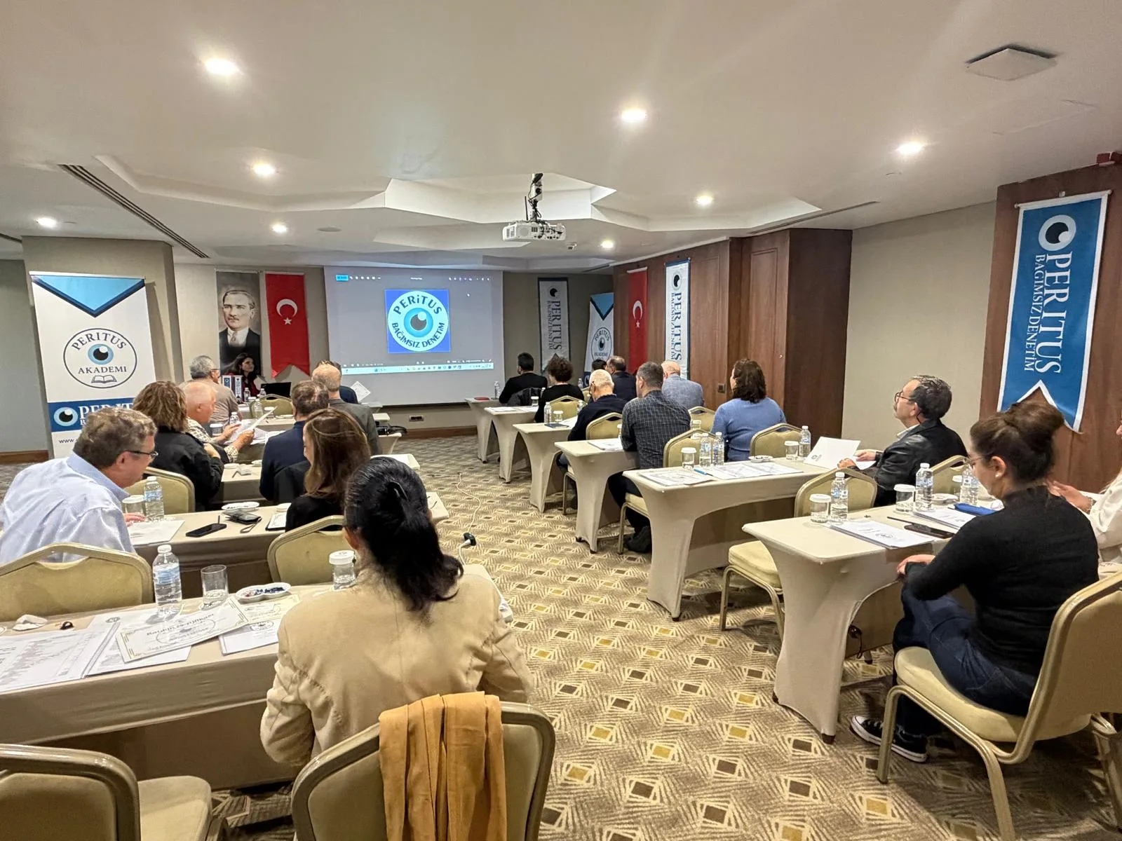 Peritus Akademi eğitim salonunda katılımcılar ve ekranda Peritus logosu